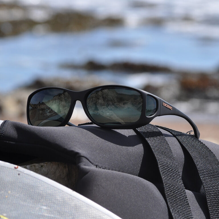 A pair of Style Line Cocoons sunglasses with photochromic gray lenses resting on a surfboard, ready for a day of surfing.